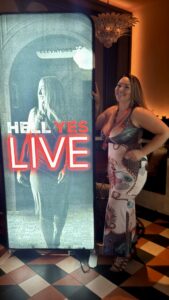 Crystle stands next to a sign for a business conference called Hell Yes Live